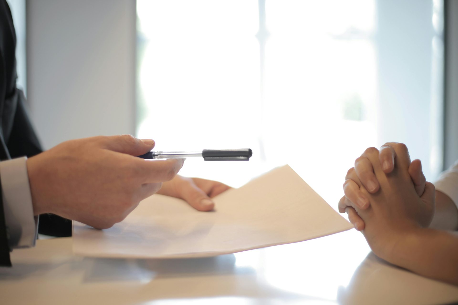 Person offering pen over contract papers.