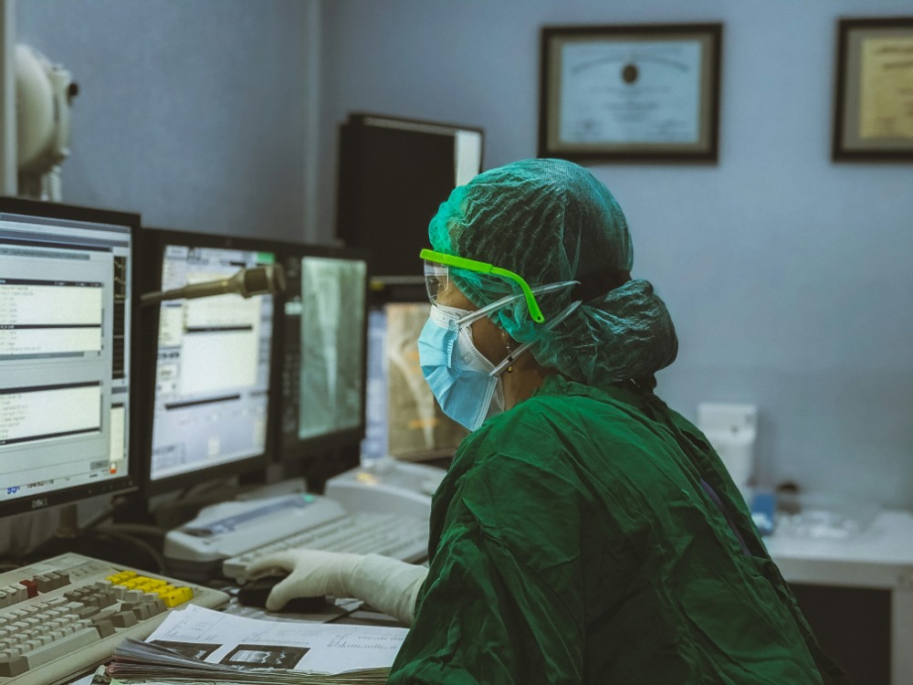 Healthcare worker monitoring data on multiple screens.