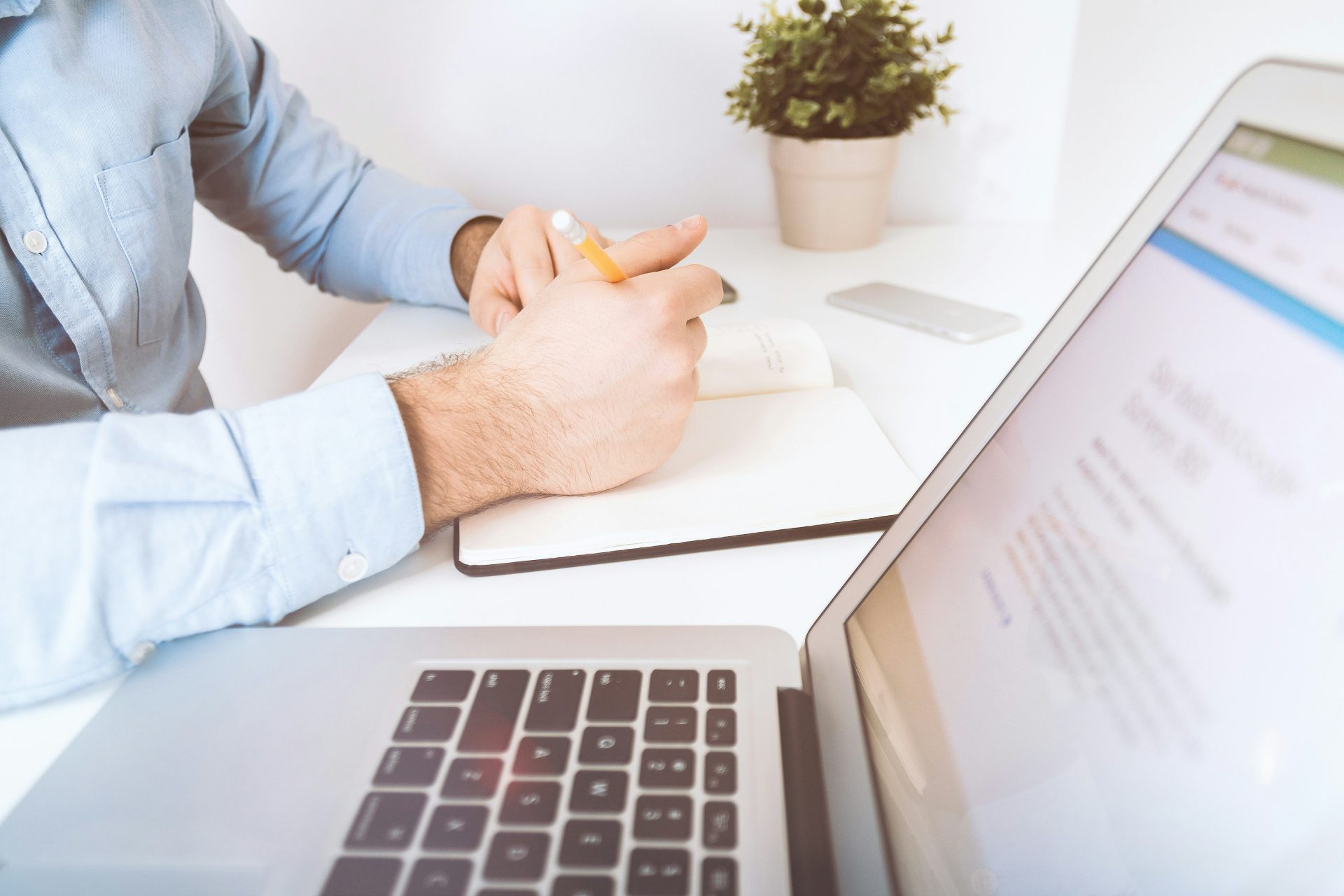 Man writing notes beside open laptop.