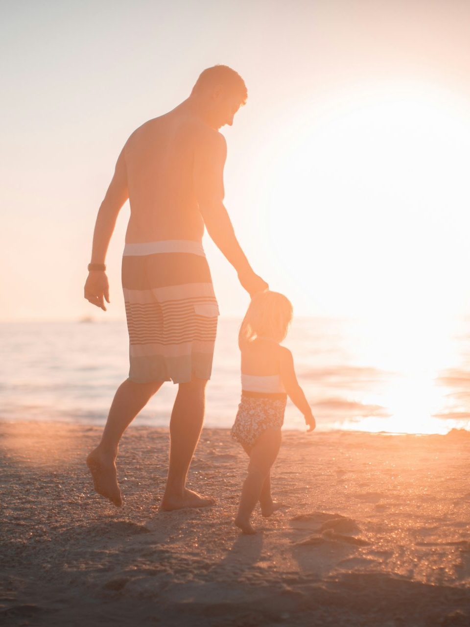 Father and daughter walking on beach sunset.