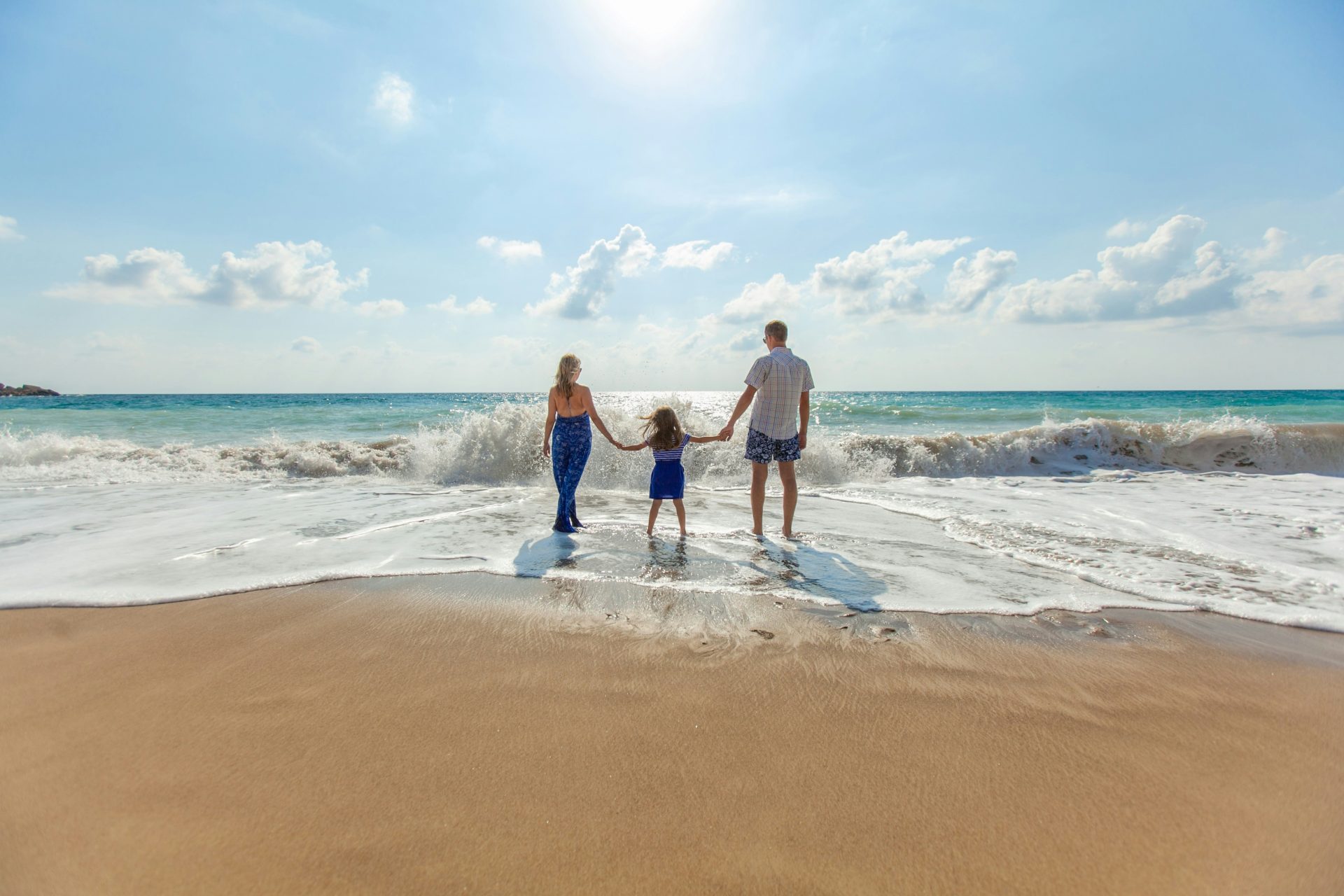 Family holding hands on sandy beach shore.